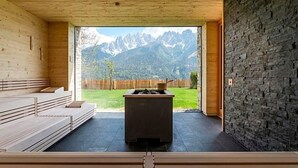 A sauna room with wooden benches, a stone wall, and a view of mountains. - Berghotel Schopfenhof (Dobbiaco)