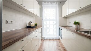 A modern kitchen with white cabinets, wooden countertops, and a window with a sheer curtain. - Warszawa Rakowska Homely Apartment (Warszawa)
