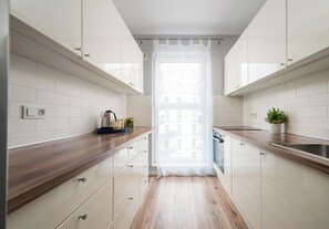A modern kitchen with white cabinets, wooden countertops, and a window with a sheer curtain. - Warszawa Rakowska Homely Apartment (Warszawa)