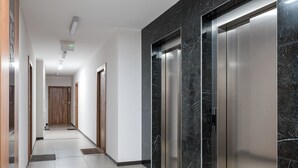 A modern hallway with a marble wall, an elevator, and a door at the end. - Warszawa Rakowska Homely Apartment (Warszawa)