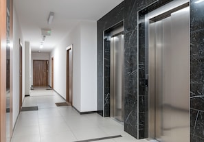 A modern hallway with a marble wall, an elevator, and a door at the end. - Warszawa Rakowska Homely Apartment (Warszawa)