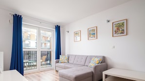 A modern living room with a grey sectional sofa, a white table, and a large window with blue curtains. - Warszawa Rakowska Homely Apartment (Warszawa)