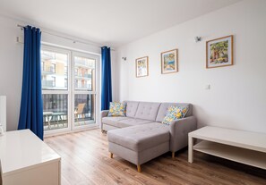 A modern living room with a grey sectional sofa, a white table, and a large window with blue curtains. - Warszawa Rakowska Homely Apartment (Warszawa)