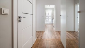 A hallway with wooden flooring, white walls, and a door with a handle. - Warszawa Rakowska Homely Apartment (Warszawa)