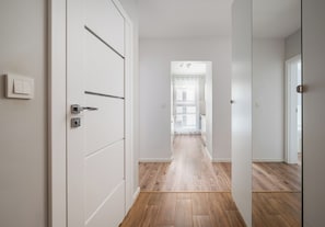 A hallway with wooden flooring, white walls, and a door with a handle. - Warszawa Rakowska Homely Apartment (Warszawa)
