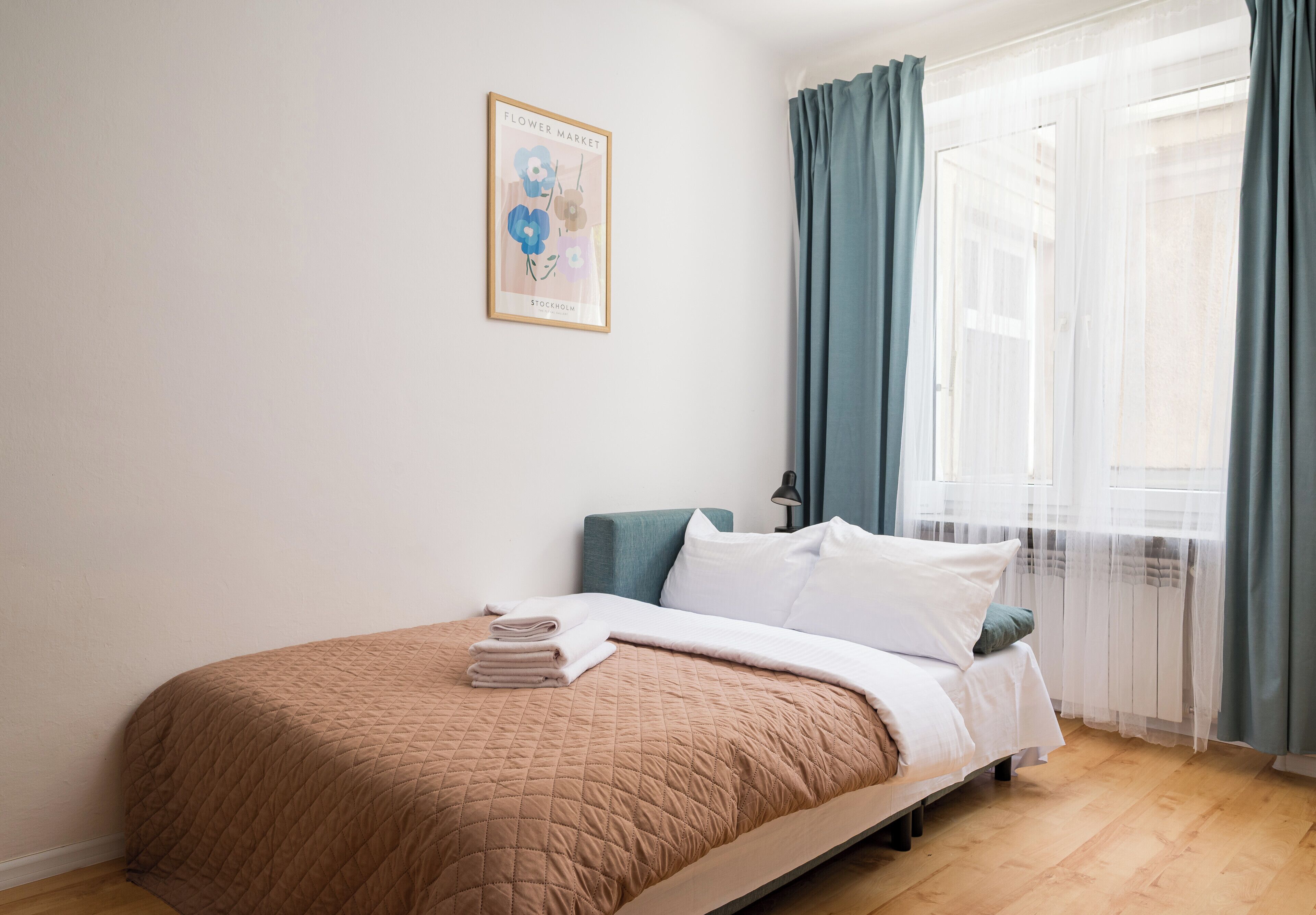 A bedroom with a bed, a framed picture on the wall, and a window with curtains.
