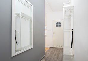 Ein Flur mit grauer Wand, einer weißen Tür mit Fenster und einem weißen Metallregal.