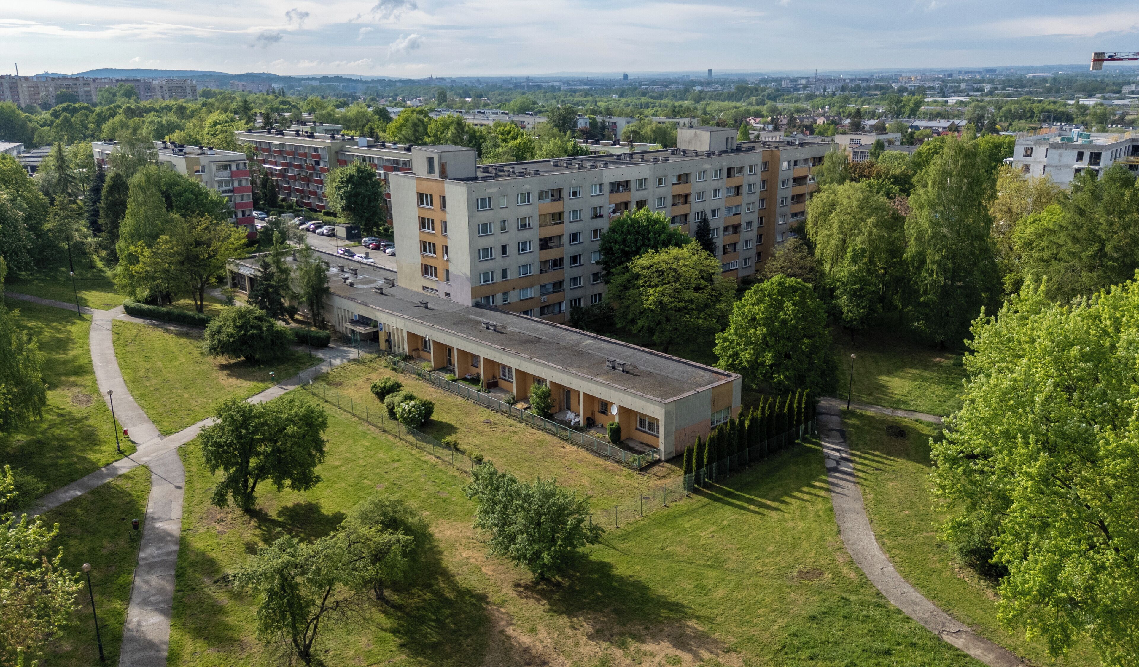 A multi-story residential building with a central courtyard, surrounded by greenery and a clear sky.