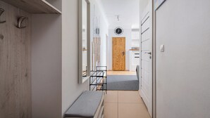 Ein schmaler Flur mit einer Bank, einer Holztür und einer Uhr an der Wand.