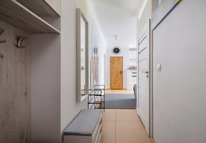 Ein schmaler Flur mit einer Bank, einer Holztür und einer Uhr an der Wand.