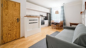 Eine moderne Wohnung mit Holztür, weißen Schränken, einer Küche mit Kühlschrank, einem Essbereich mit Tisch und Stühlen sowie einem grauen Sofa.