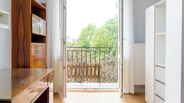 Ein Zimmer mit Holzschrank, Glastisch, weißem Kleiderschrank und einem Balkon mit Metallgeländer.