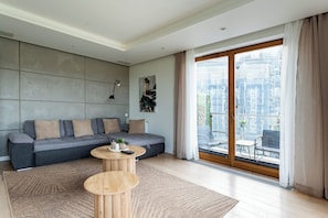 A modern living room with a grey sofa, a small wooden table, and a large sliding glass door leading to an outdoor balcony. - Taneczna Spacious Apartment (Gdańsk)