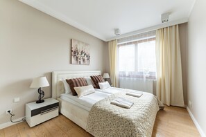 A hotel room with a bed, bedside tables, a lamp, a painting, and a window with curtains. - Taneczna Spacious Apartment (Gdańsk)