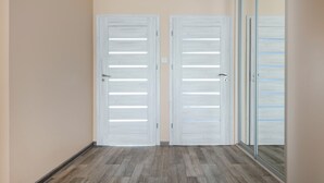 A hallway with two white doors and a glass door, wooden flooring, and a beige wall.