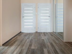 Un couloir avec deux portes blanches et une porte en verre, un plancher en bois et un mur de couleur beige.