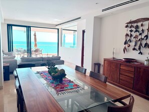 Ein moderner Essbereich mit einem Glastisch, einem Holzschrank und Blick auf das Meer.