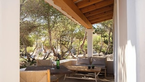 An outdoor patio with a wooden table, wicker chairs, a sofa, and a view of trees and hills. - Las Dunas Apt (Formentera)