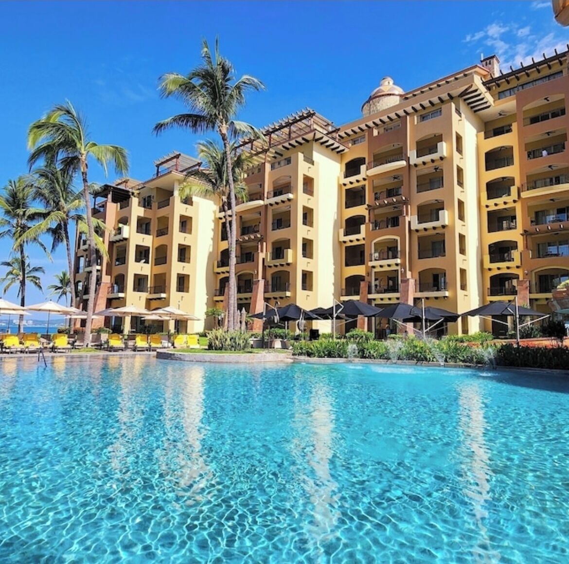 A hotel with a pool, palm trees, and a clear blue sky.