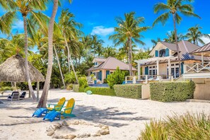 Una propiedad frente a la playa con una casa grande, palmeras y sillas de playa.