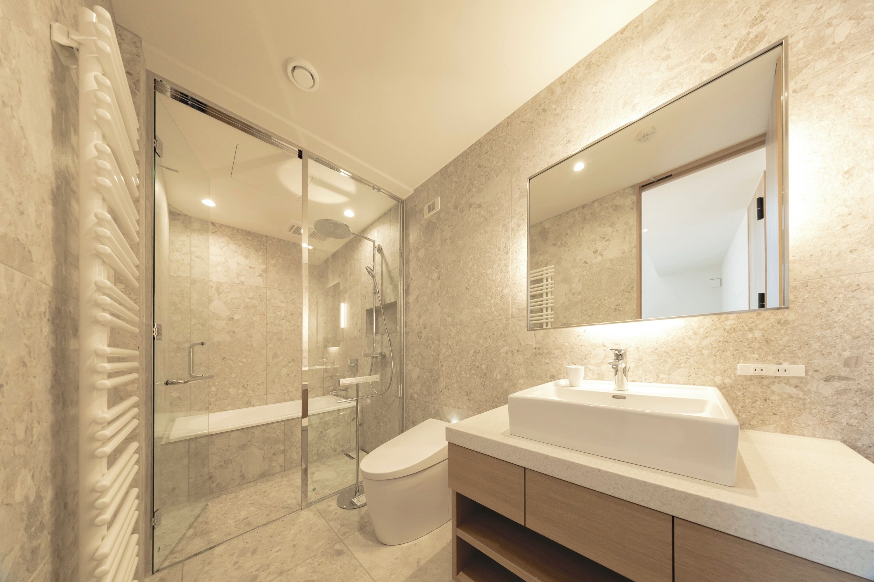 Une salle de bain moderne avec une douche à l’italienne en verre, un lavabo blanc et un grand miroir.