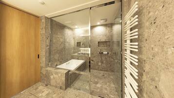 A modern bathroom with a glass shower enclosure, a wooden door, and a marble-tiled floor.