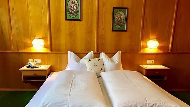 Un lit double avec du linge de lit blanc, deux tables de chevet avec des lampes et des motifs floraux décorant les murs.