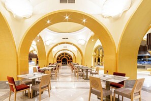 A spacious hotel dining area with multiple tables and chairs, high ceilings with star-shaped lighting, and a central arched entrance. - Grand Resort (Hurghada)