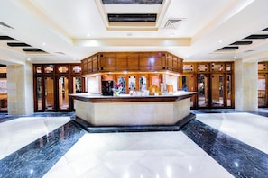 A hotel lobby with a central reception desk, marble flooring, and wooden paneling. - Grand Resort (Hurghada)