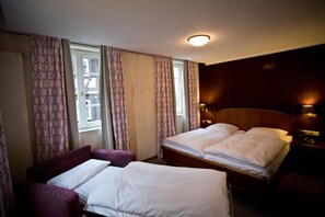Hotellihuone, jossa on parivuode, kaksi erillistä sänkyä, sohva, työpöytä ja ikkuna, jossa on verhot.
