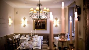 A formal dining room with a long table set for a meal, a chandelier, wall sconces, and a painting on the wall. - Karpfen (Eberbach)