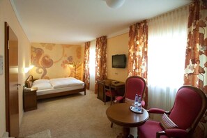 Hotellihuone, jossa on sänky, työpöytä, tuoli, televisio ja pöytä, jonka päällä on pullo.