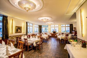A spacious dining area with multiple tables, elegant chandeliers, and large windows providing natural light. - Karpfen (Eberbach)