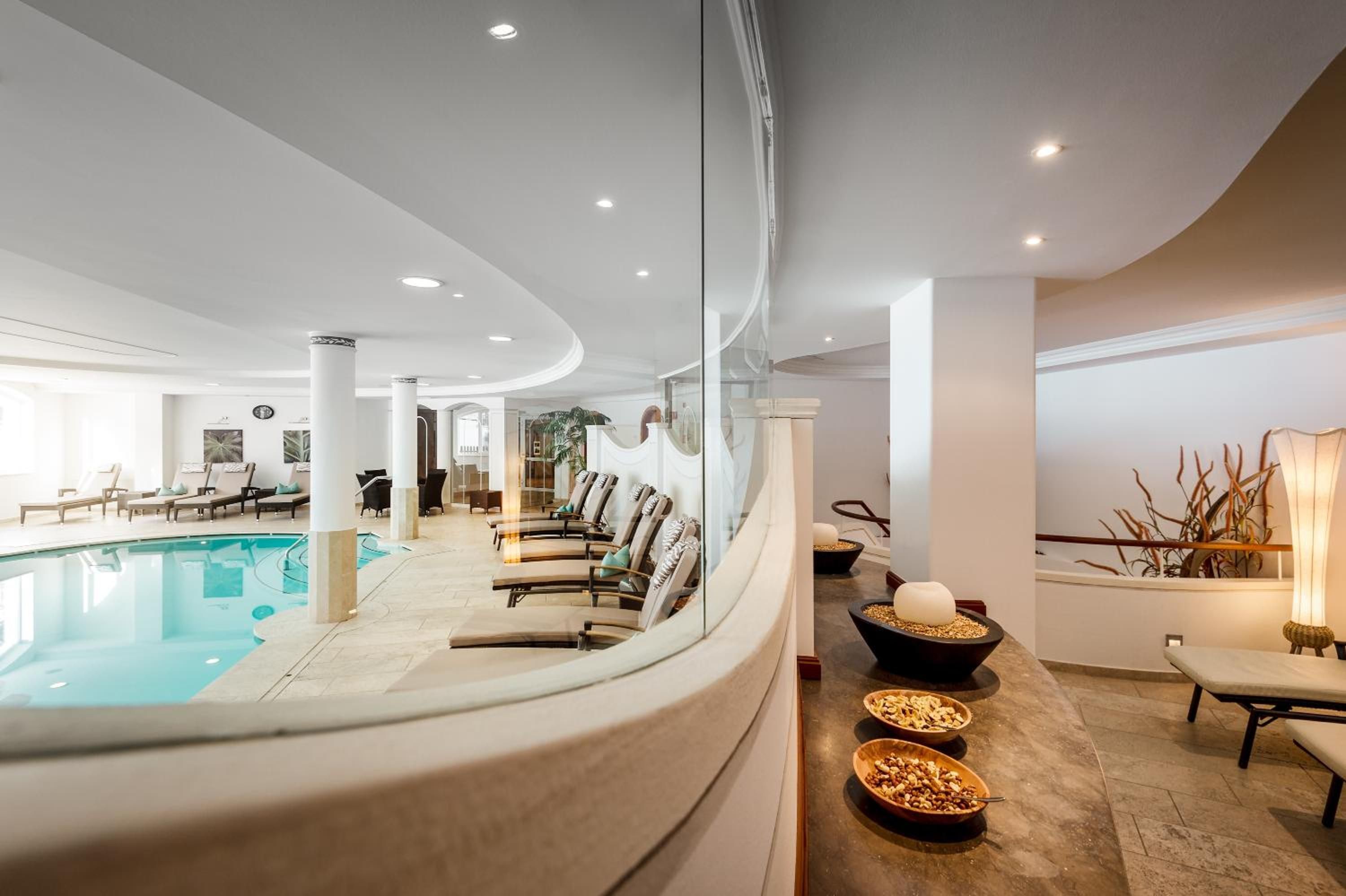 Ein moderner Poolbereich im Innenbereich mit Liegestühlen, einer Rezeption und einem Essbereich mit Schalen voller Nüsse.
