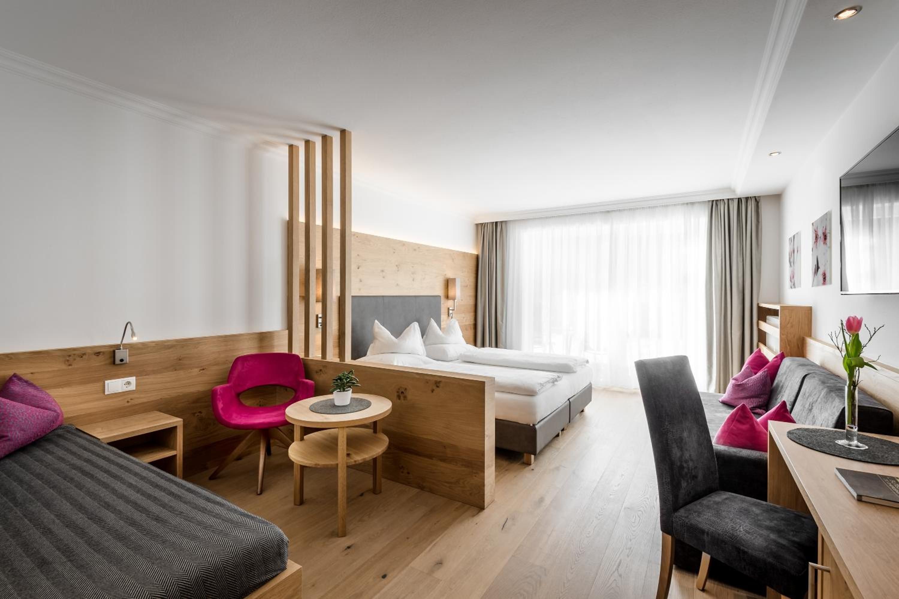 Moderni hotellihuone, jossa on sänky, työpöytä, tuoli, pieni pöytä ja sohva.