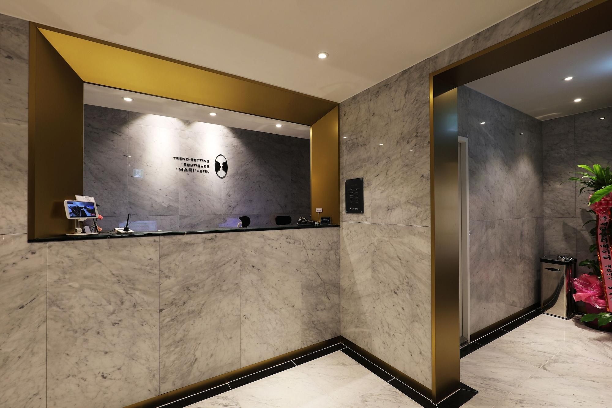 Een receptiegedeelte met een marmeren wand, een receptiebalie, een digitaal scherm en een bordje met 'Trend-Setting Boutiques Mari Hotel'.