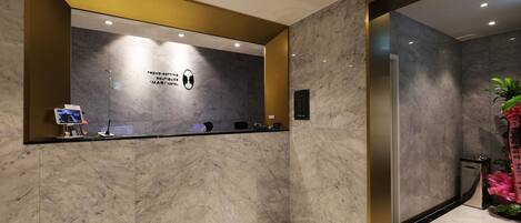 Een receptiegedeelte met een marmeren wand, een receptiebalie, een digitaal scherm en een bordje met 'Trend-Setting Boutiques Mari Hotel'.
