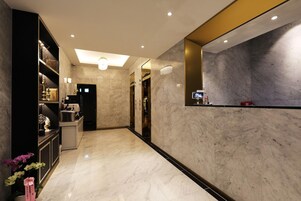 Vestíbulo de hotel con suelo de mármol, mostrador de recepción, escalera e iluminación empotrada en el techo.