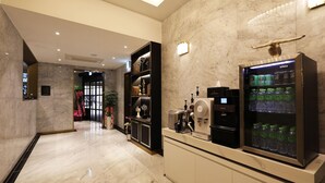 Rebedor d'hotel amb sòl de marbre, taulell de recepció, barra minibar i dispensador d'aigua.