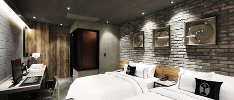 A hotel room with a brick wall, two beds, a desk with a computer, and a shower area.