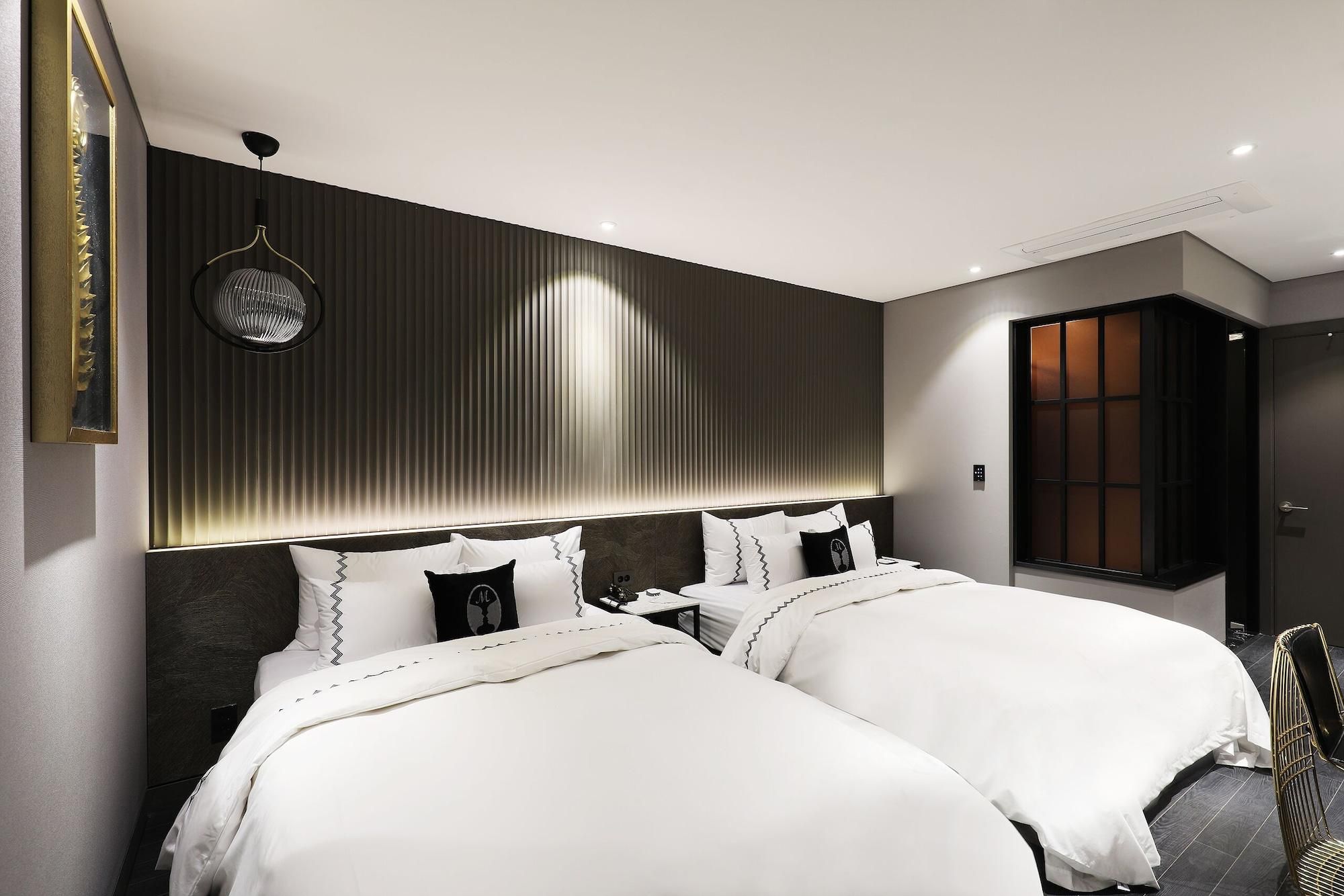 Ein modernes Hotelzimmer mit zwei Betten, einem großen Spiegel, einer Wandleuchte und einer Schiebetür.