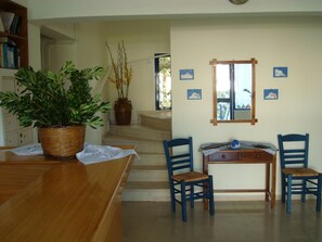 Un comedor con una mesa de madera, sillas, una planta en maceta, un jarrón y una escalera que conduce a otra habitación.