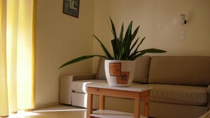 A living room with a sofa, a small wooden table, and a potted plant. - Philippos Studios & Apartments (Kos)