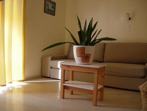 A living room with a sofa, a small wooden table, and a potted plant. - Philippos Studios & Apartments (Kos)