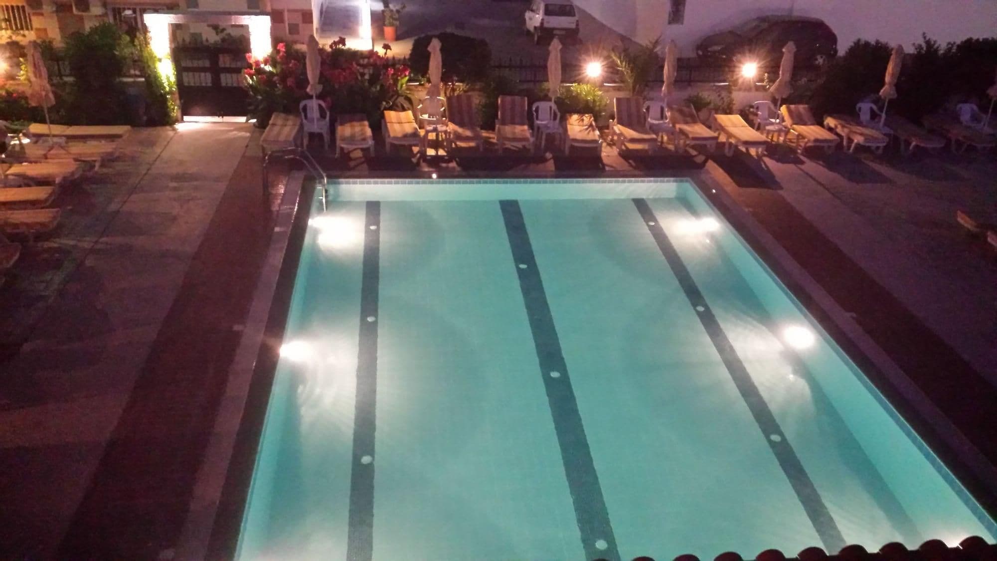 Una piscina con sillones de descanso y sombrillas, rodeada por un área pavimentada.