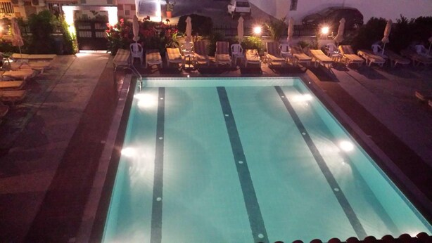 A swimming pool with lounge chairs and umbrellas, surrounded by a paved area. - Philippos Studios & Apartments (Kos)