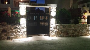 A stone gate with a metal gate, illuminated by lights, leading to a building with a stone wall and potted plants. - Philippos Studios & Apartments (Kos)
