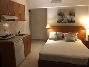A bedroom with a bed, pillows, a nightstand with a lamp, and a painting on the wall. - Philippos Studios & Apartments (Kos)