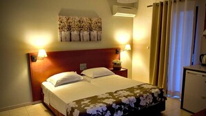 A hotel room with a bed, two bedside lamps, a wall-mounted air conditioner, a small table with a vase, and a desk with a kettle. - Philippos Studios & Apartments (Kos)