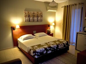 A hotel room with a bed, two bedside lamps, a wall-mounted air conditioner, a small table with a vase, and a desk with a kettle. - Philippos Studios & Apartments (Kos)